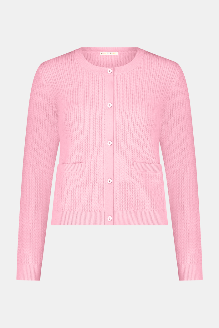 A woman with long brown hair models the Roller Rabbit Laine Cardigan—a cotton candy pink style with white buttons and front pockets—paired with a white and yellow plaid skirt with floral accents, set against a plain light background.
