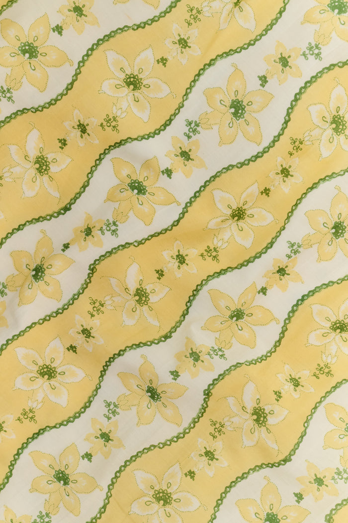 A woman wearing the Roller Rabbit Lillian Floral Stripe Briella Dress, featuring a retro-inspired yellow floral print and puffed sleeves, stands facing the camera and smiles slightly against a plain white background.