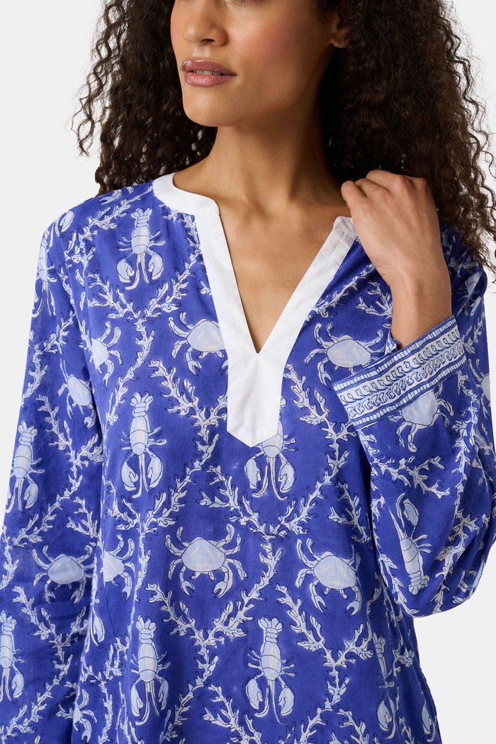 A woman wears the Roller Rabbit Lobster Trellis Johanna Caftan in blue and white, featuring a white V-neckline and hem, paired with sandals against a plain background.