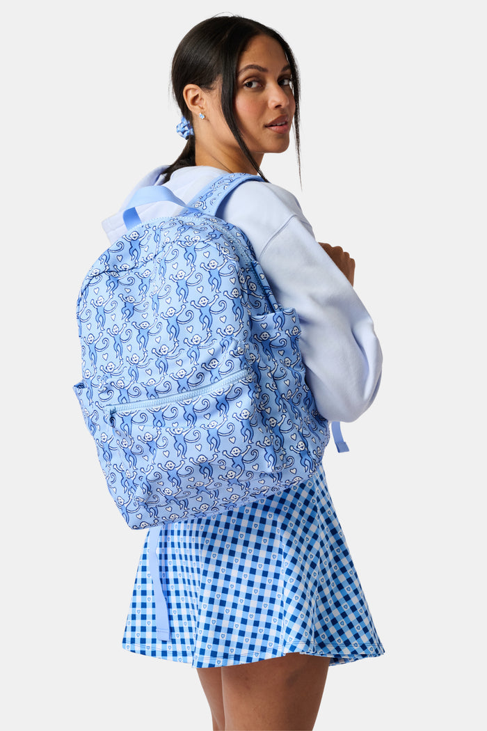 The Roller Rabbit Lovely Monkey Backpack for kids features a playful pattern of monkeys in various poses, a front pocket, and pink zippers set against a light background.