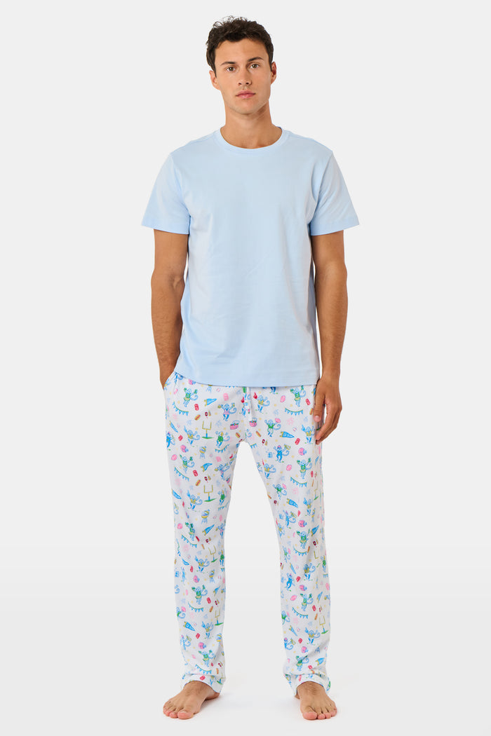 The Mens Game Day Troy Pajamas set by Roller Rabbit features a light blue short-sleeve t-shirt paired with white pajama pants decorated with colorful, playful cartoon animal and toy prints. The set is displayed on a plain white background.