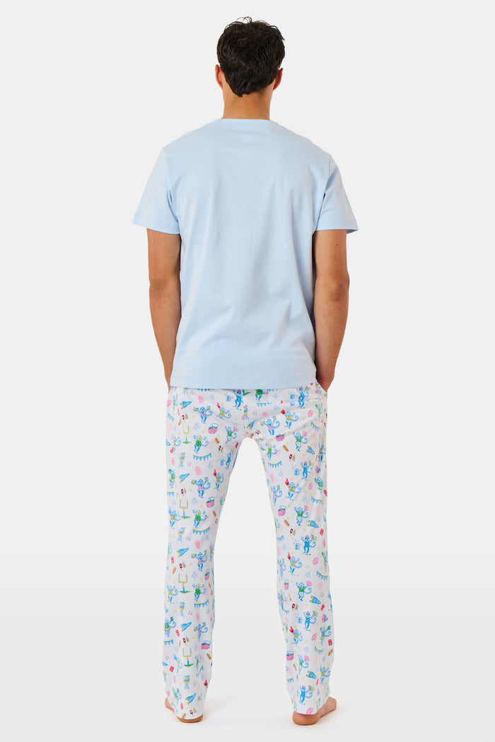 The Mens Game Day Troy Pajamas set by Roller Rabbit features a light blue short-sleeve t-shirt paired with white pajama pants decorated with colorful, playful cartoon animal and toy prints. The set is displayed on a plain white background.