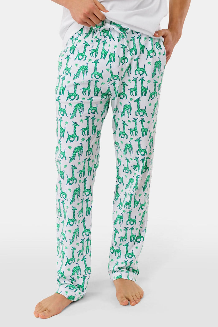 A person wears Roller Rabbit's Mens Gigi Giraffe Simon Pant, white pajama pants with a giraffe print, standing barefoot against a plain white background. Made from 100 Pima Cotton, the pull-on style features a hand in the pocket and a partially visible upper body.