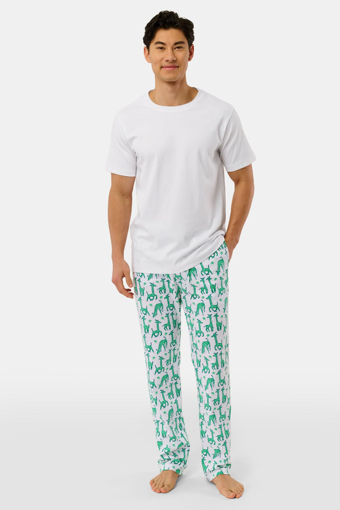 A person wears Roller Rabbit's Mens Gigi Giraffe Simon Pant, white pajama pants with a giraffe print, standing barefoot against a plain white background. Made from 100 Pima Cotton, the pull-on style features a hand in the pocket and a partially visible upper body.