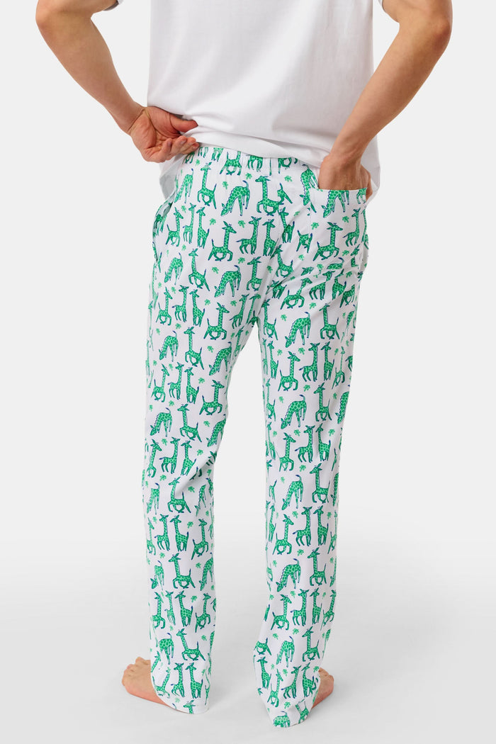 A person wears Roller Rabbit's Mens Gigi Giraffe Simon Pant, white pajama pants with a giraffe print, standing barefoot against a plain white background. Made from 100 Pima Cotton, the pull-on style features a hand in the pocket and a partially visible upper body.