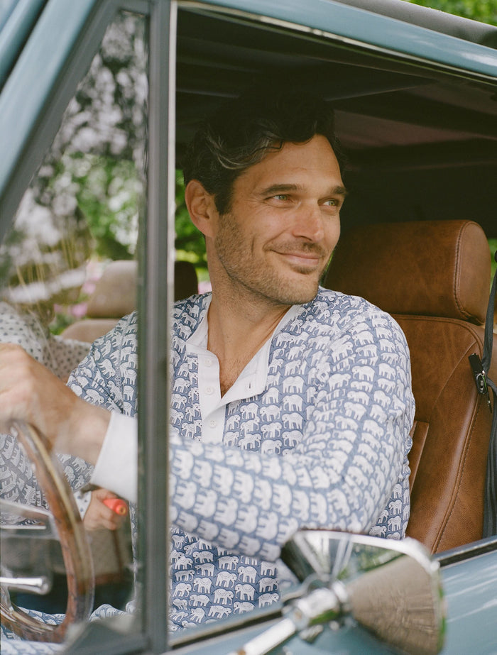 A man stands barefoot in Roller Rabbit's Mens Hathi Spencer Pajamas, a blue and white long-sleeve set with a small pattern and buttoned collar, made from 100 Pima Cotton, against a plain white background.