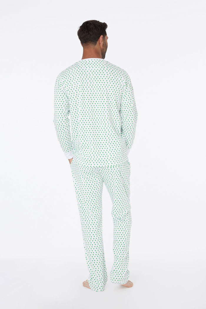 A man stands barefoot and smiling in Roller Rabbit Mens Hearts Spencer Pajamas with an Emerald Hearts print, long sleeves, and 100 Pima cotton, against a plain white background.
