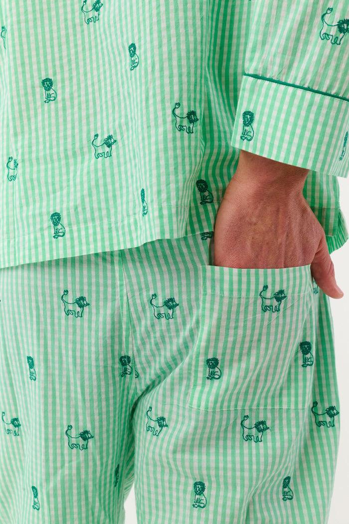 A man stands barefoot against a white background, smiling and facing forward, wearing Roller Rabbit's Mens Leo Gingham Loungewear—a light green, long-sleeved button-up set with matching pants featuring a small lion print pattern.