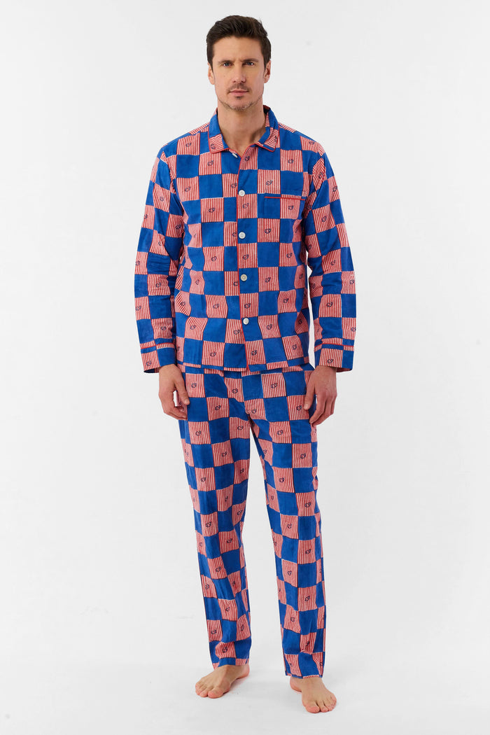 A man with short brown hair and a neutral expression stands barefoot against a white background, wearing the Roller Rabbit Mens Moby Grand Prix Loungewear set in blue and pink checkered cotton with long sleeves and pants.
