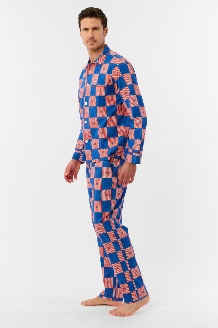 A man with short brown hair and a neutral expression stands barefoot against a white background, wearing the Roller Rabbit Mens Moby Grand Prix Loungewear set in blue and pink checkered cotton with long sleeves and pants.