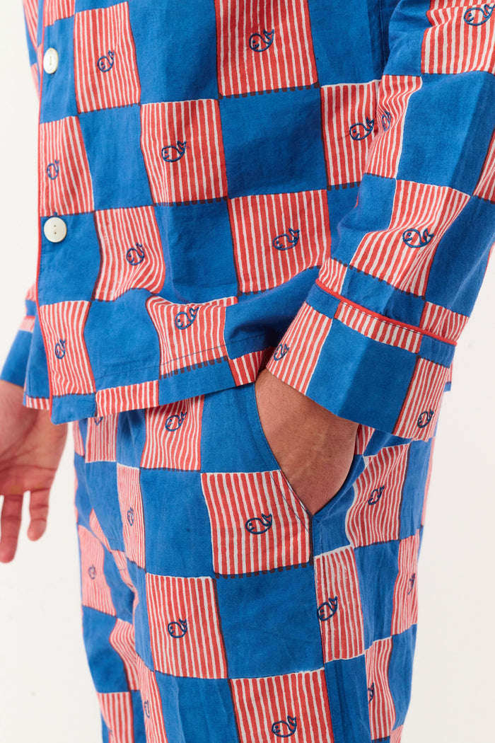 A man with short brown hair and a neutral expression stands barefoot against a white background, wearing the Roller Rabbit Mens Moby Grand Prix Loungewear set in blue and pink checkered cotton with long sleeves and pants.