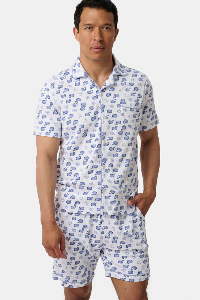 A man stands barefoot facing forward in Roller Rabbit’s Mens Moby Louie Pajamas—a Pima cotton set with blue patterns on white, featuring a short-sleeve button-up shirt and shorts—against a plain white background.