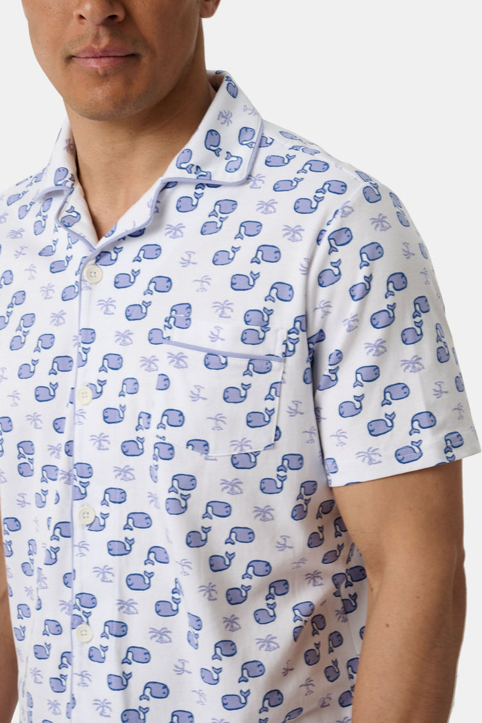 A man stands barefoot facing forward in Roller Rabbit’s Mens Moby Louie Pajamas—a Pima cotton set with blue patterns on white, featuring a short-sleeve button-up shirt and shorts—against a plain white background.