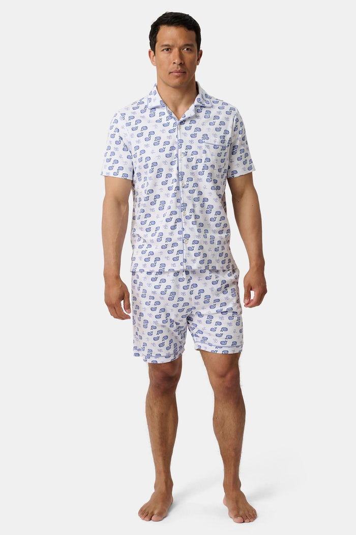 A man stands barefoot facing forward in Roller Rabbit’s Mens Moby Louie Pajamas—a Pima cotton set with blue patterns on white, featuring a short-sleeve button-up shirt and shorts—against a plain white background.