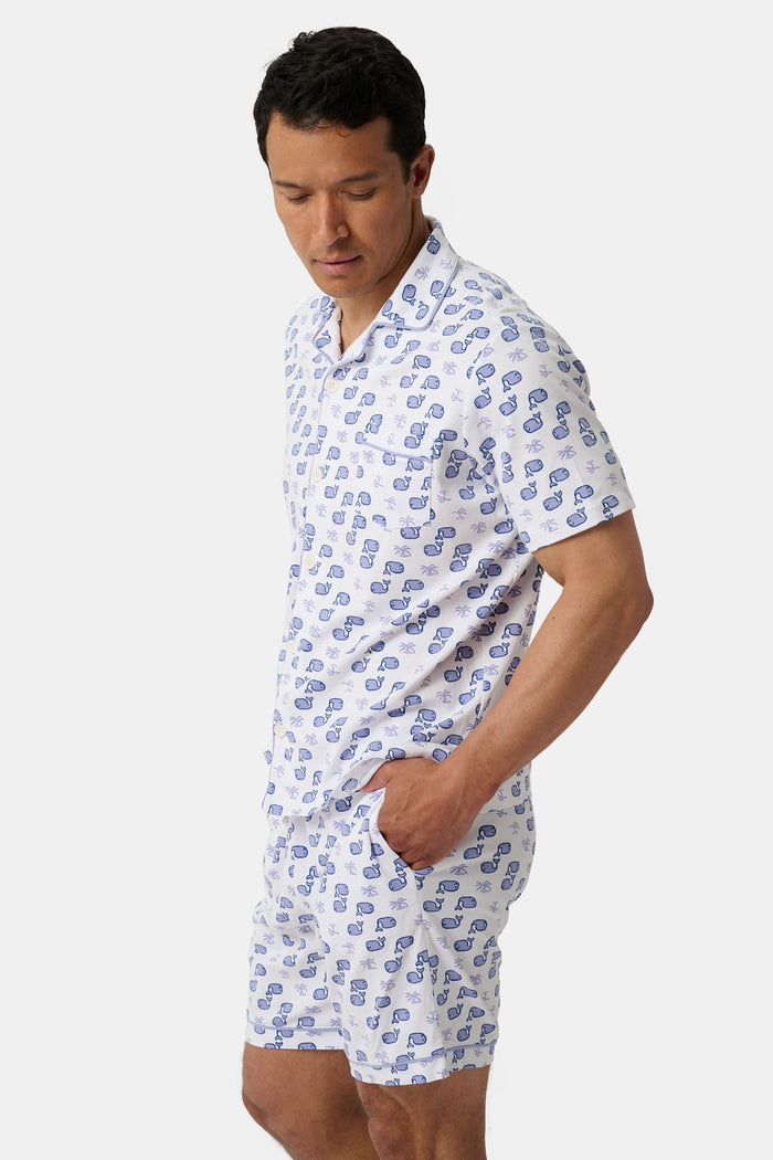 A man stands barefoot facing forward in Roller Rabbit’s Mens Moby Louie Pajamas—a Pima cotton set with blue patterns on white, featuring a short-sleeve button-up shirt and shorts—against a plain white background.