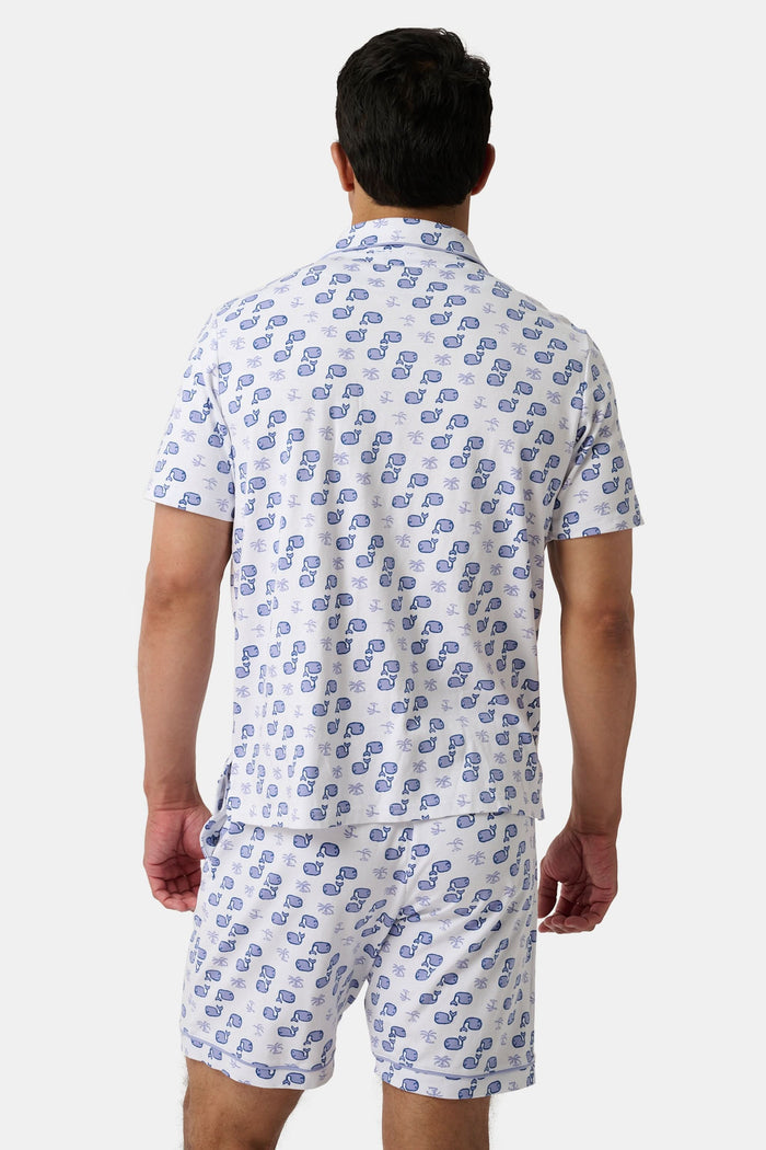A man stands barefoot facing forward in Roller Rabbit’s Mens Moby Louie Pajamas—a Pima cotton set with blue patterns on white, featuring a short-sleeve button-up shirt and shorts—against a plain white background.