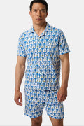 A man stands barefoot against a white background wearing Roller Rabbit Mens Monkey Louie Pajamas—a matching short-sleeve button-up shirt and shorts featuring a blue and white abstract print in 100 Pima cotton.
