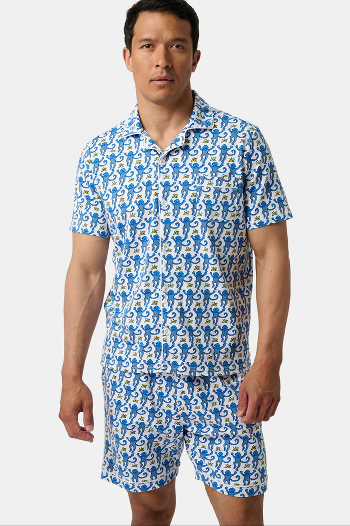 A man stands barefoot against a white background wearing Roller Rabbit Mens Monkey Louie Pajamas—a matching short-sleeve button-up shirt and shorts featuring a blue and white abstract print in 100 Pima cotton.