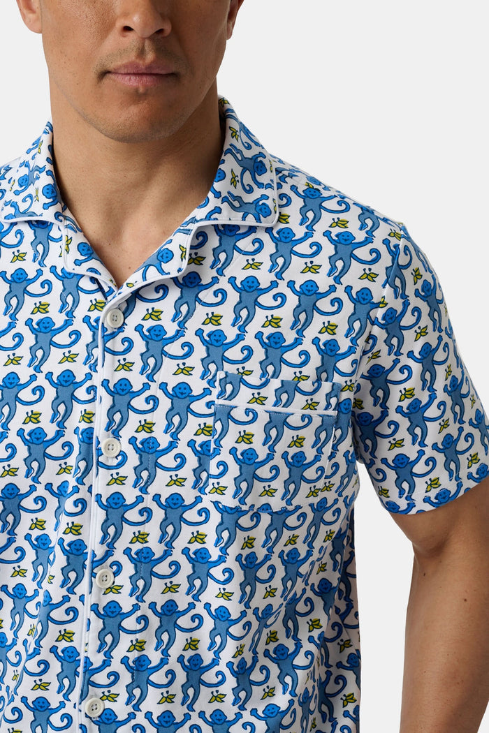 A man stands barefoot against a white background wearing Roller Rabbit Mens Monkey Louie Pajamas—a matching short-sleeve button-up shirt and shorts featuring a blue and white abstract print in 100 Pima cotton.