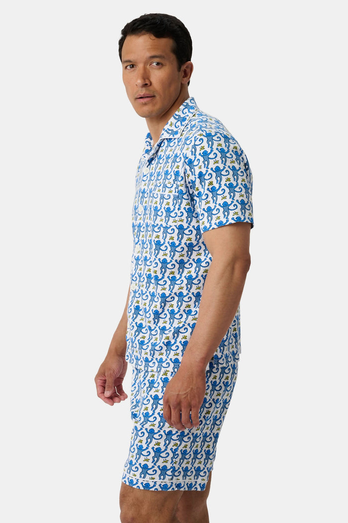 A man stands barefoot against a white background wearing Roller Rabbit Mens Monkey Louie Pajamas—a matching short-sleeve button-up shirt and shorts featuring a blue and white abstract print in 100 Pima cotton.