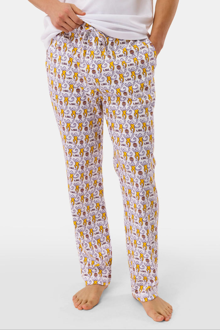 A man with short dark hair stands barefoot against a plain background, wearing a white t-shirt and Roller Rabbit Mens Tigers Lovely Monkey Simon Pant lounge pants with a yellow and brown design. He has a relaxed, neutral expression.