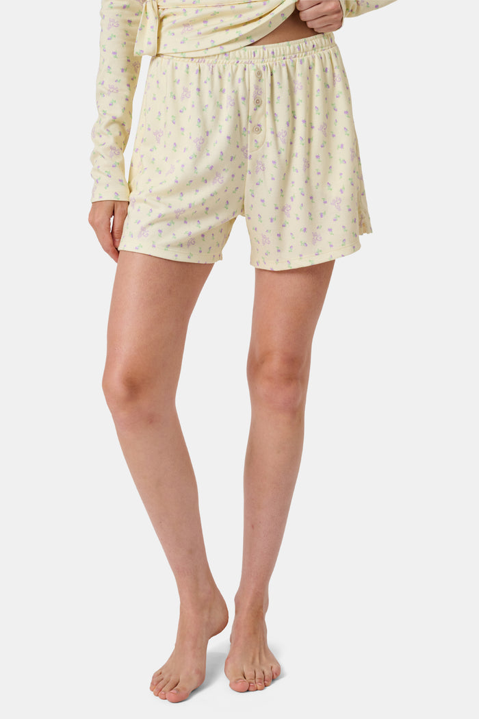 The Mini Monkey Blossom Brooklyn Boxer by Roller Rabbit features light yellow Pima cotton with a delicate pastel floral print and an elastic waistband. Displayed on a plain white background, these comfortable women’s loungewear sleep shorts are perfect for relaxing at home.