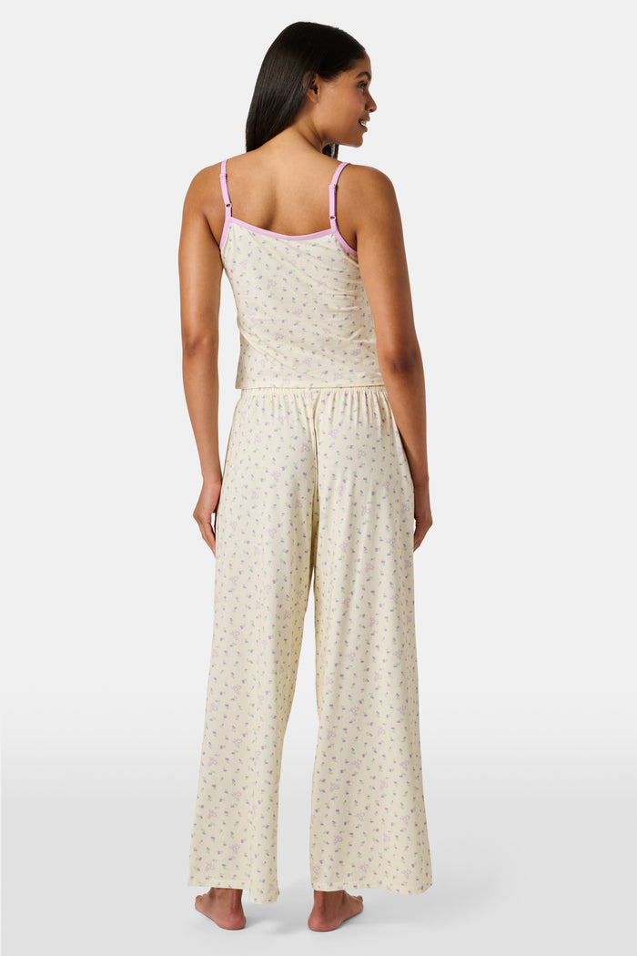 A yellow Mini Monkey Blossom Clarkson Cami by Roller Rabbit, featuring spaghetti straps, a small floral print, and purple trim along the neckline and straps, displayed on a plain white background. This camisole pairs perfectly with the Monroe Lounge Pant for a coordinated look.