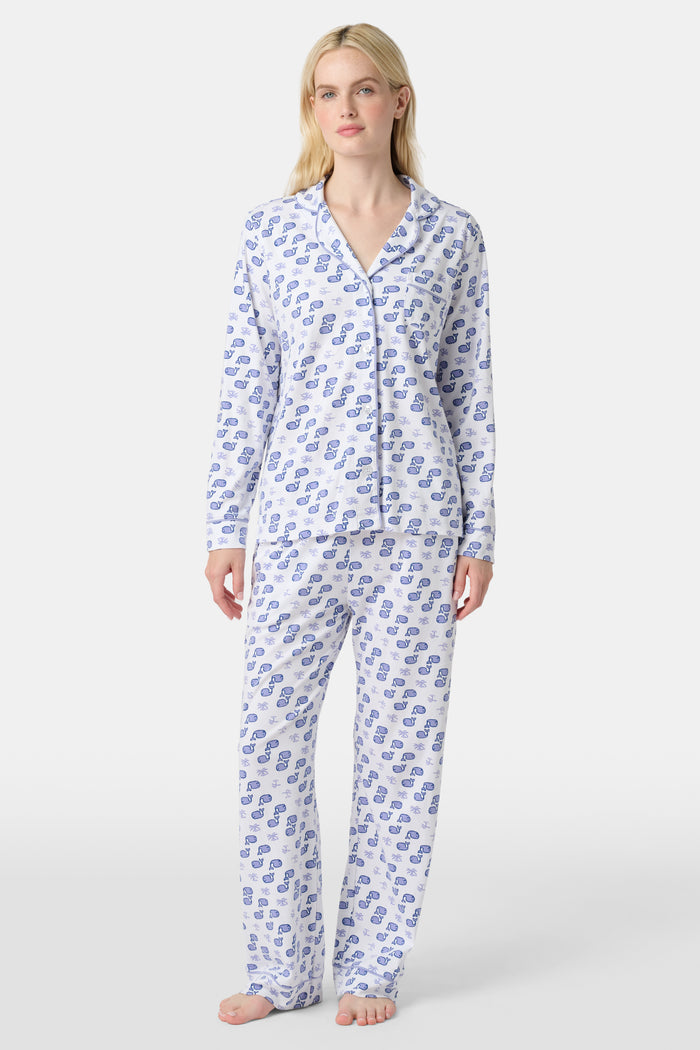 A woman stands barefoot in the Roller Rabbit Moby Long Sleeve Polo Pajamas, featuring a blue geometric-patterned white top and pants. Made from soft pima cotton, the comfy set is shown against a plain white background.