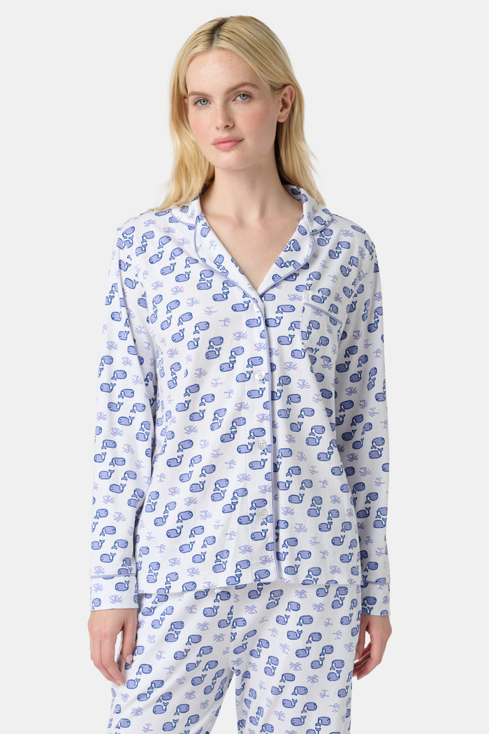 A woman stands barefoot in the Roller Rabbit Moby Long Sleeve Polo Pajamas, featuring a blue geometric-patterned white top and pants. Made from soft pima cotton, the comfy set is shown against a plain white background.