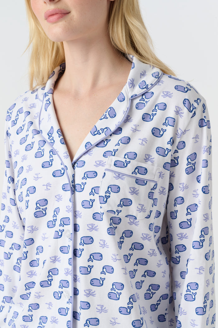 A woman stands barefoot in the Roller Rabbit Moby Long Sleeve Polo Pajamas, featuring a blue geometric-patterned white top and pants. Made from soft pima cotton, the comfy set is shown against a plain white background.