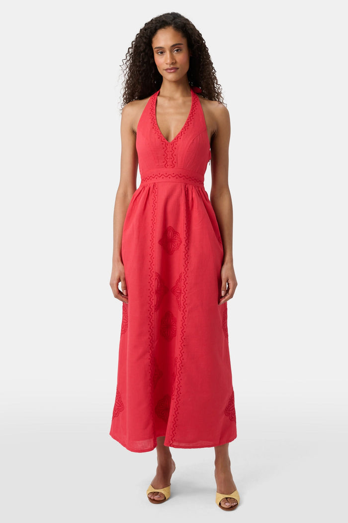 A woman with long curly hair wears the Roller Rabbit Monaco Geo Penelope Dress, a sleeveless, halter-neck, ankle-length red dress with subtle embroidery. She stands forward in open-toed, low-heeled sandals against a plain white background.