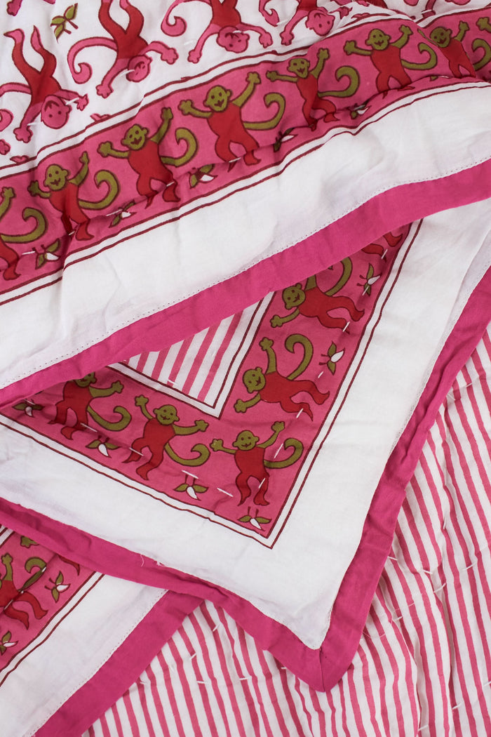 The Monkey Baby Quilt by Roller Rabbit is a soft cotton quilt with a pink and white floral pattern, green accents, intricate pink designs, a contrasting pink border, and a decorative patch in one corner.
