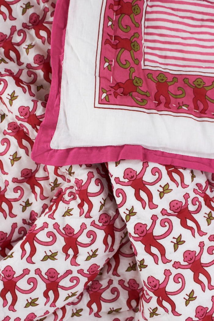 The Monkey Baby Quilt by Roller Rabbit is a soft cotton quilt with a pink and white floral pattern, green accents, intricate pink designs, a contrasting pink border, and a decorative patch in one corner.