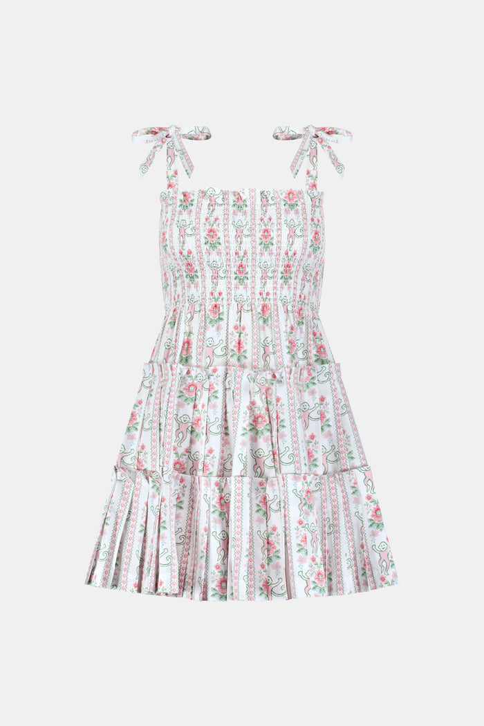 A young woman wears the Roller Rabbit Monkey Block Stripe Ribbon Charlotte Nap Dress, featuring a smocked bodice, ruffled hem, and tied shoulder straps. Her straight hair is partly tied back with a matching ribbon against a plain white background.