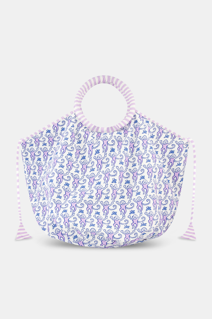 The Roller Rabbit Monkey Bondi Bag is a spacious cotton canvas tote with purple and white wavy stripe handles and drawstrings, featuring a blue and purple abstract floral print on a white background.