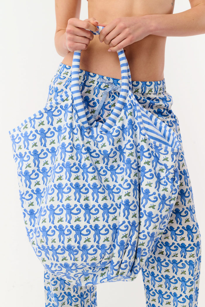 The SAPPHIRE Monkey Bondi Bag is a large cotton canvas tote with blue and white floral patterns, round striped handles, and drawstring ties—ideal for weekend getaways. Shown against a plain light background.