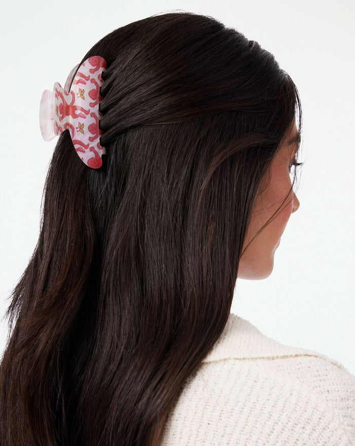 The Roller Rabbit Monkey Claw Clip is a butterfly-shaped hair accessory with a white base, decorated with playful pink monkeys holding yellow leaves.