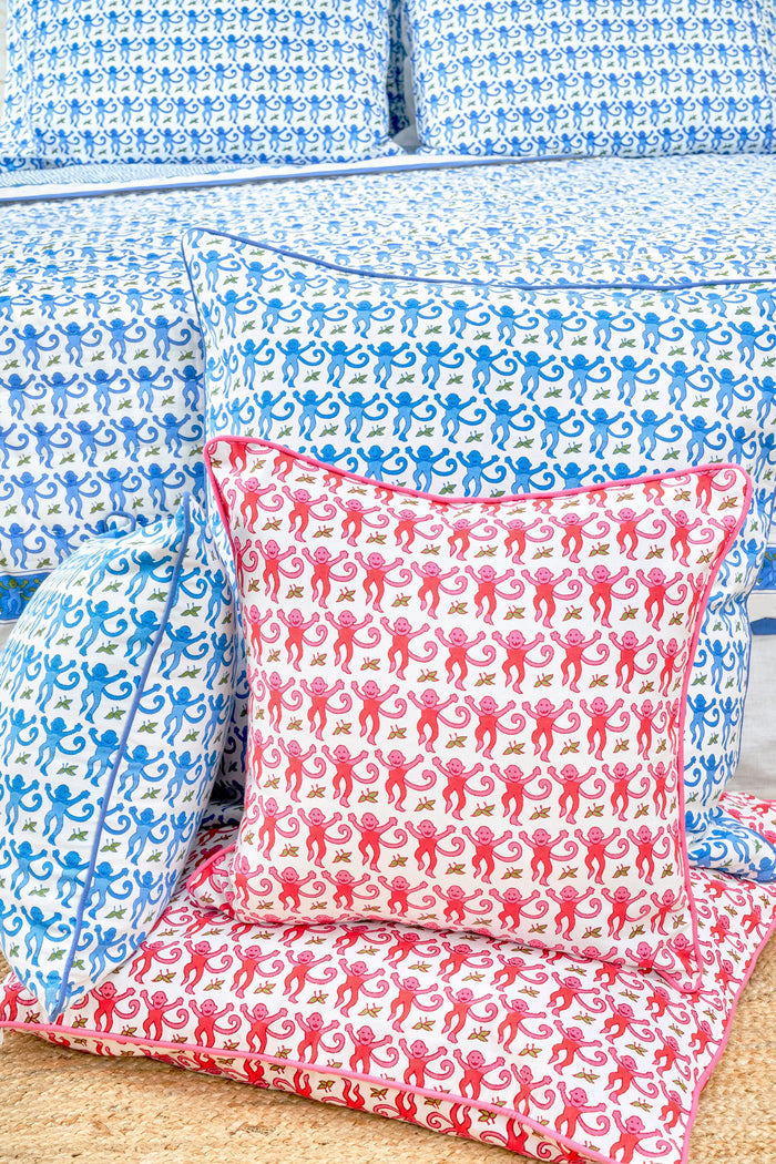 The Roller Rabbit Monkey Decorative Pillow features a white background with a repeating blue monkey and green leaf pattern, finished with a blue piped edge. This cotton pillow adds playful charm to any space.