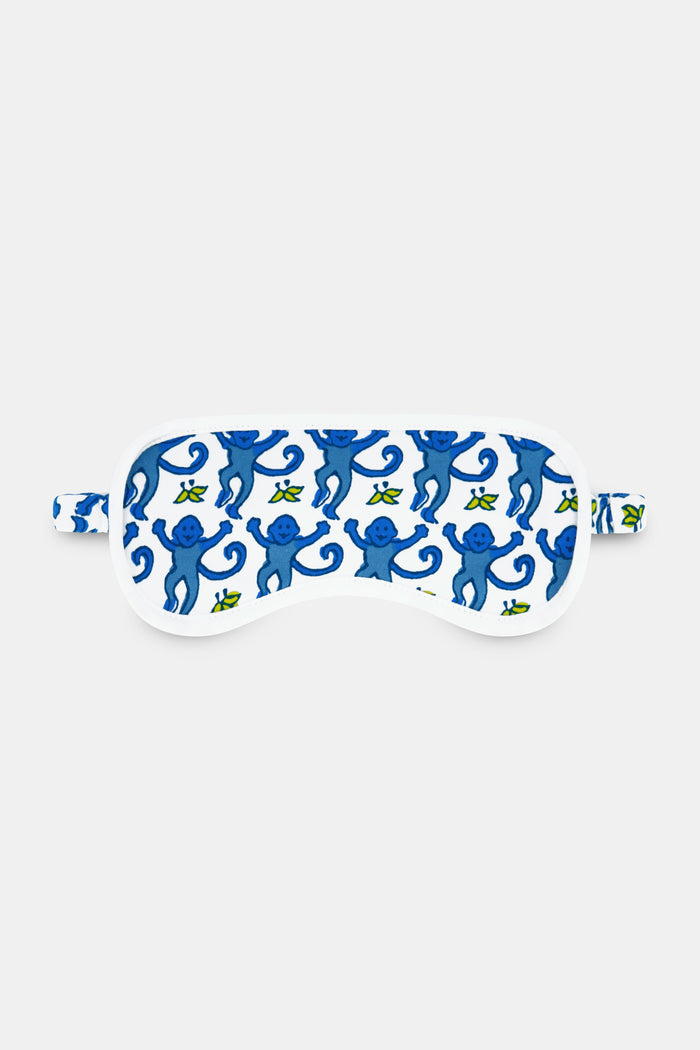 The Roller Rabbit Monkey Eye Mask is crafted from soft Pima cotton and features a white base with blue monkeys, small green bananas, and a matching strap.