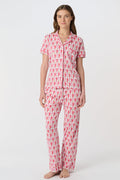 A woman stands barefoot against a plain white background, wearing the Roller Rabbit Monkey Fiora Pajamas set, which features a short-sleeve, button-up top and long pants.