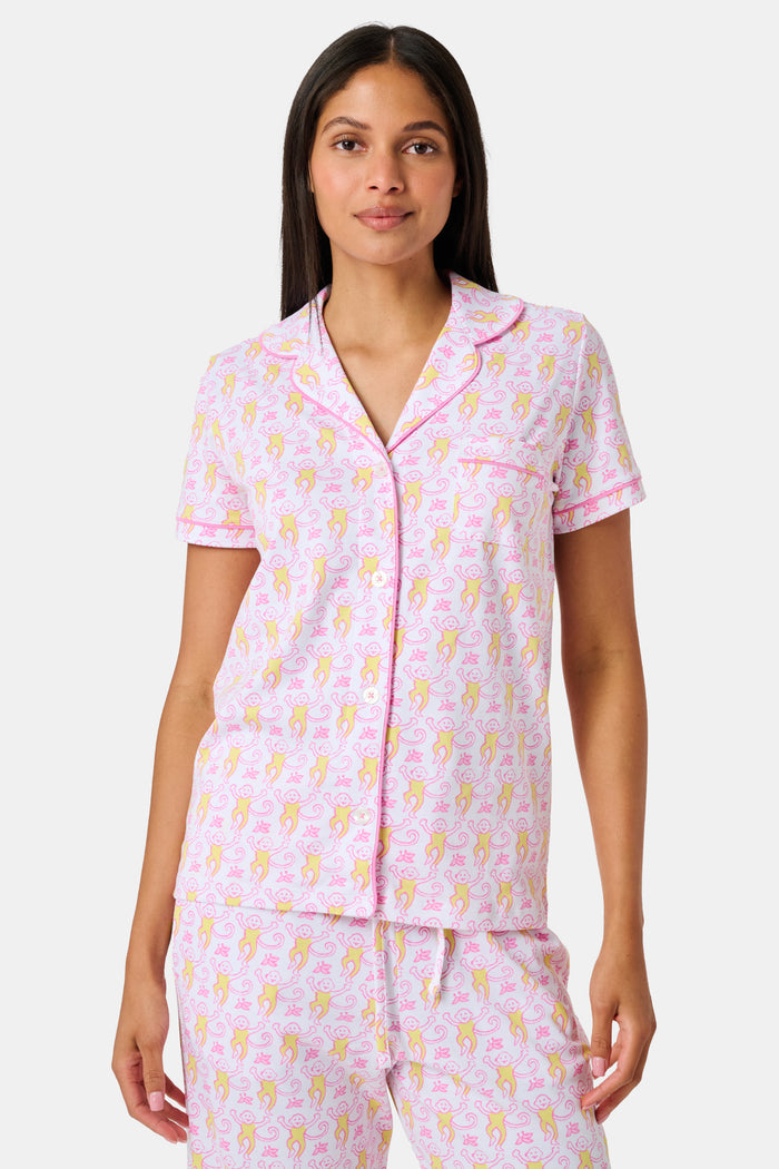 Introducing the Monkey Fiora Pajamas from Roller Rabbit—crafted from fabric adorned with a delightful pattern of pink and yellow monkeys with curled tails and smiling faces, interspersed with tiny leaves on a crisp white background. Perfect for adding playful charm to your sleepwear collection.