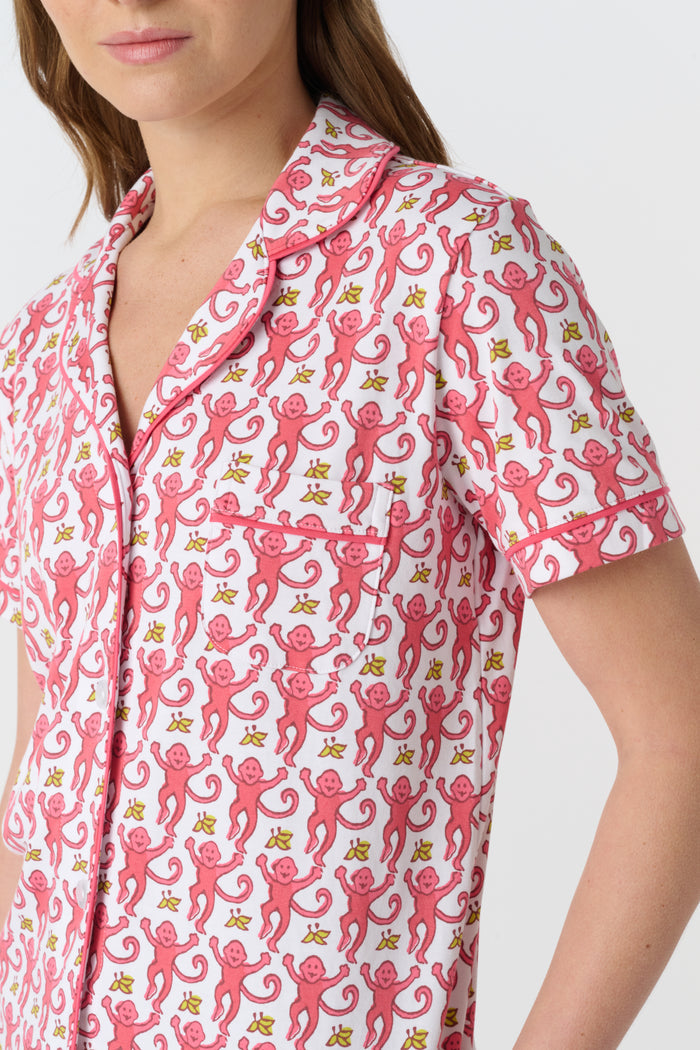 A woman stands barefoot against a plain white background, wearing the Roller Rabbit Monkey Fiora Pajamas set, which features a short-sleeve, button-up top and long pants.