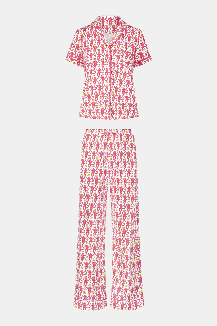 A woman stands barefoot against a plain white background, wearing the Roller Rabbit Monkey Fiora Pajamas set, which features a short-sleeve, button-up top and long pants.