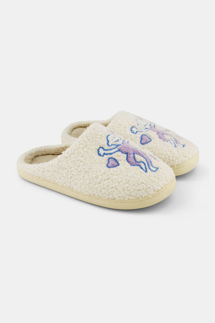 Roller Rabbit Monkey Fuzzy Slippers in cream-colored shearling feature an embroidered purple and blue bear holding two pink hearts on top, shown on a white background.