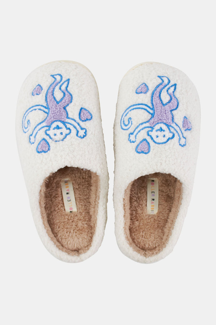 Roller Rabbit Monkey Fuzzy Slippers in cream-colored shearling feature an embroidered purple and blue bear holding two pink hearts on top, shown on a white background.