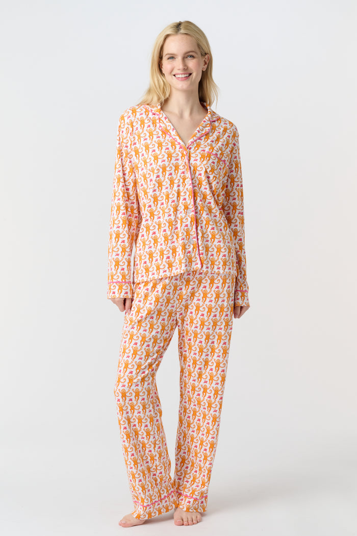 A smiling woman stands barefoot against a light background, wearing Roller Rabbit's Monkey Long Sleeve Polo Pajamas—a matching women's comfy PJs set with long sleeves and pants.