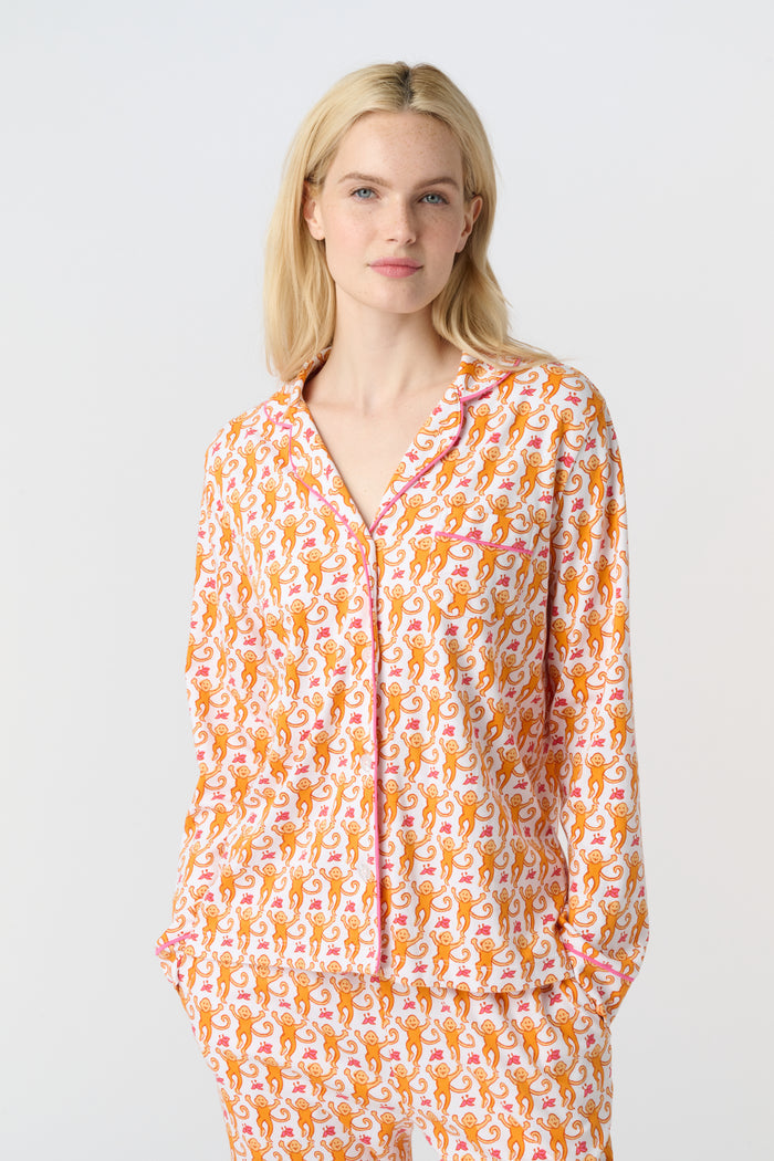 A smiling woman stands barefoot against a light background, wearing Roller Rabbit's Monkey Long Sleeve Polo Pajamas—a matching women's comfy PJs set with long sleeves and pants.