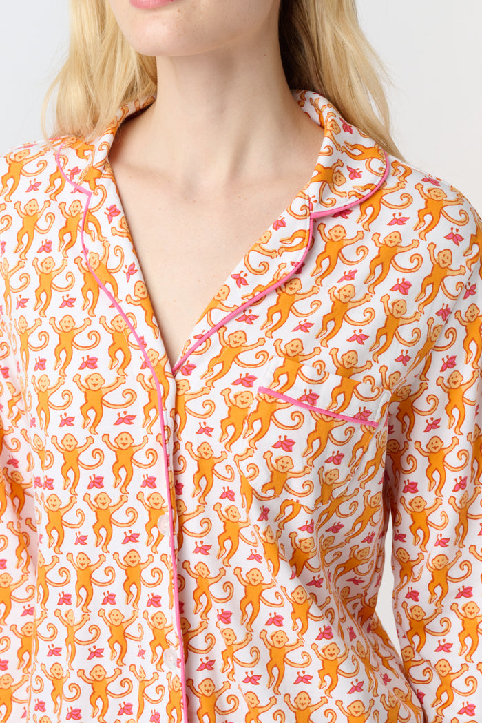 A smiling woman stands barefoot against a light background, wearing Roller Rabbit's Monkey Long Sleeve Polo Pajamas—a matching women's comfy PJs set with long sleeves and pants.