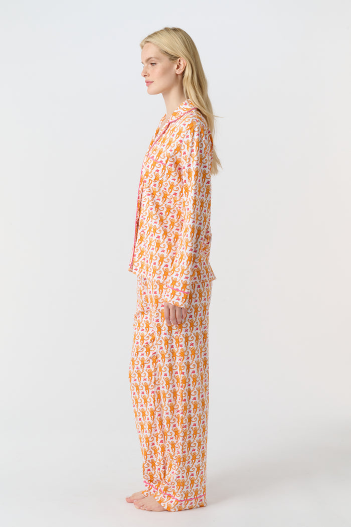 A smiling woman stands barefoot against a light background, wearing Roller Rabbit's Monkey Long Sleeve Polo Pajamas—a matching women's comfy PJs set with long sleeves and pants.