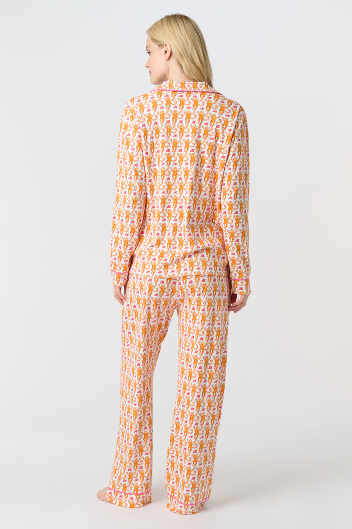 A smiling woman stands barefoot against a light background, wearing Roller Rabbit's Monkey Long Sleeve Polo Pajamas—a matching women's comfy PJs set with long sleeves and pants.